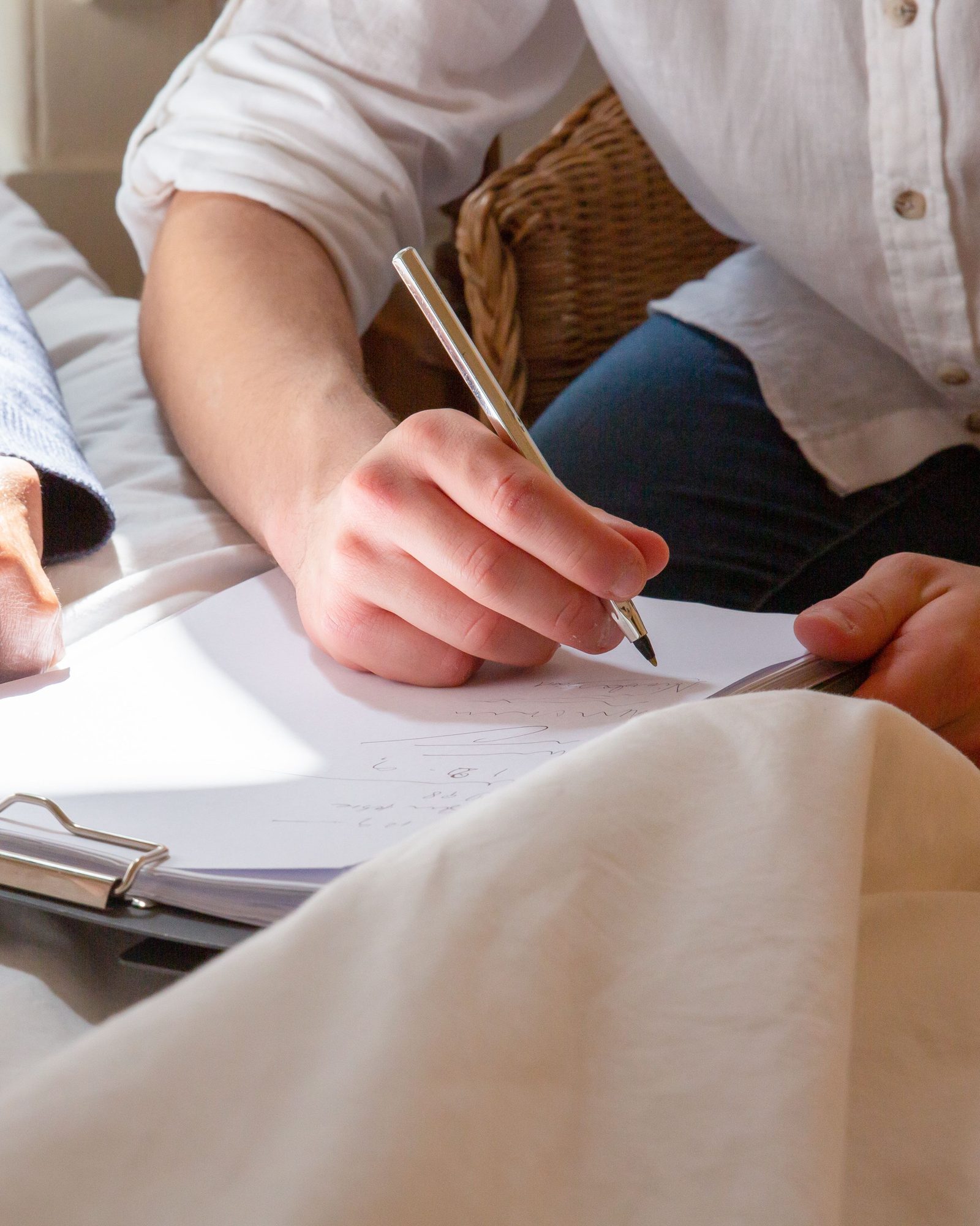 A hand filling in a form on a clipboard at a bedside